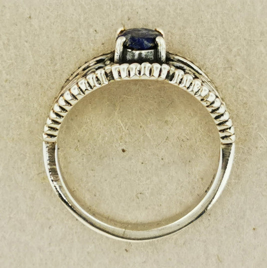 A silver ring with a blue gemstone, possibly a sapphire, set in a decorative band.