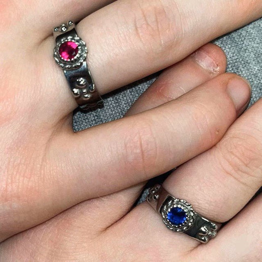 Two silver rings with gemstones are being held together by a person's fingers.