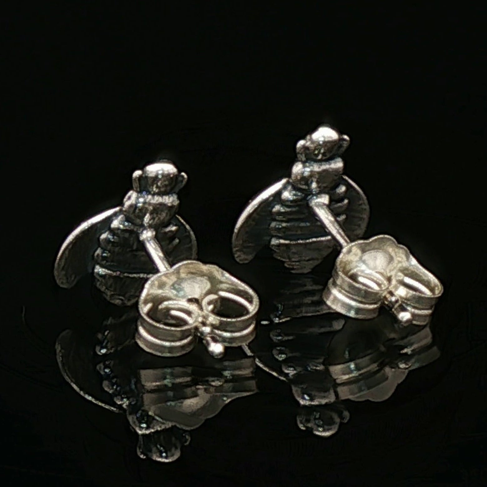Back view of silver bee-shaped earrings on a black background.