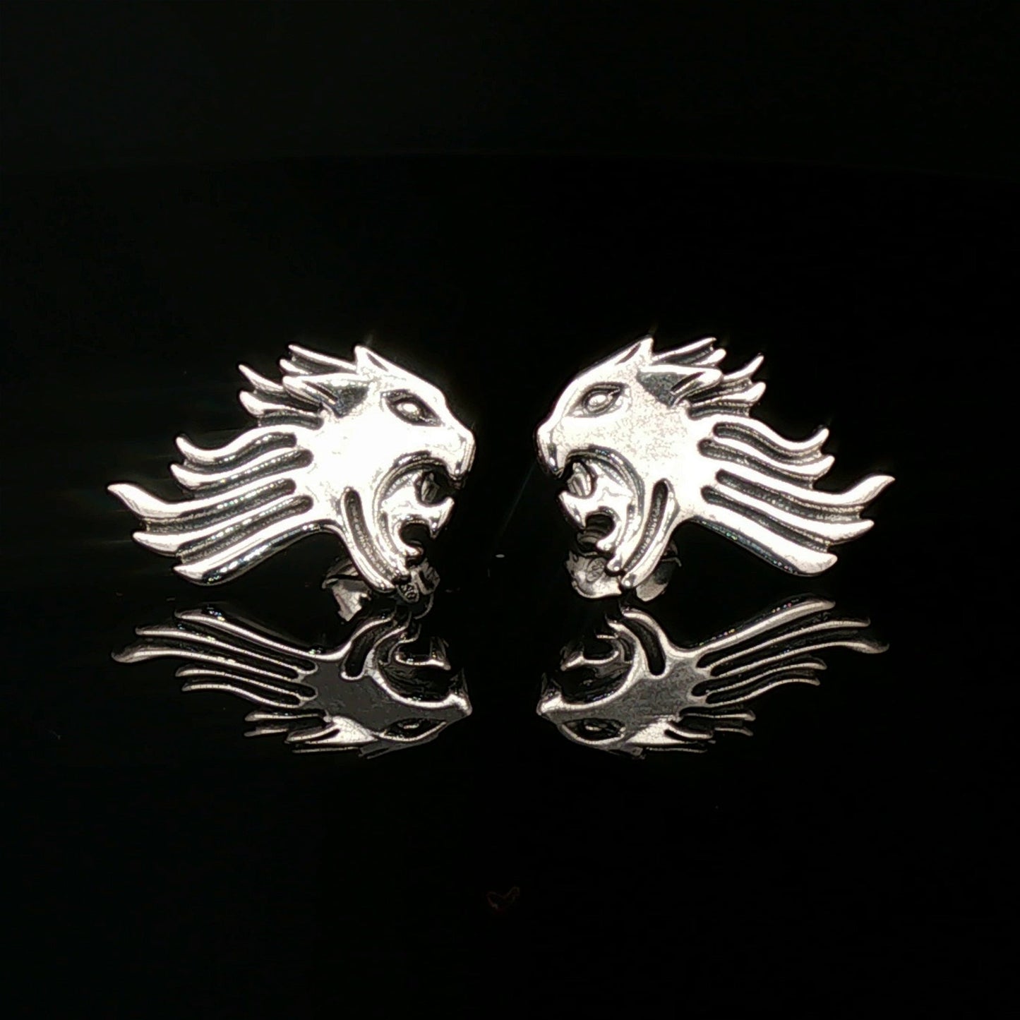 Pair of silver lion head earrings on a black background