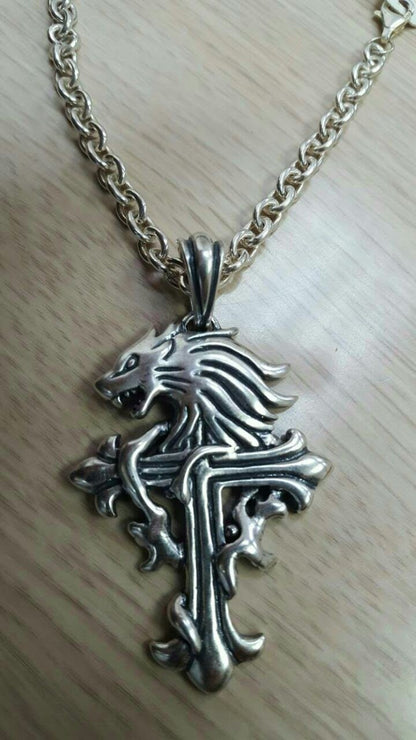 A silver-toned pendant featuring an intricate design of a lion's head with flowing mane and tail, set against a cross-like structure.