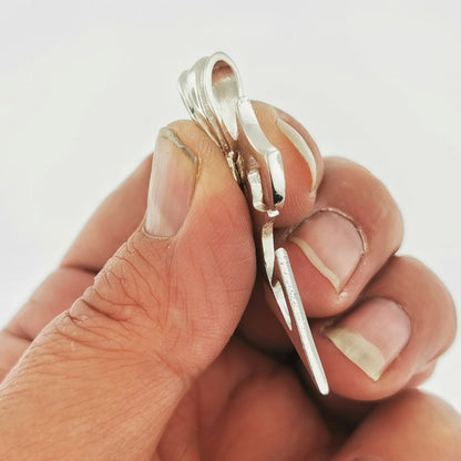 A close-up image of a person's hand holding a silver pendant or charm.