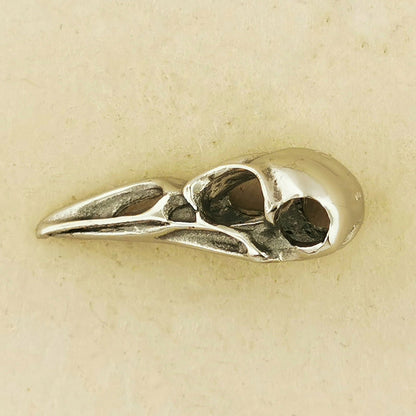 Side View of bird skull pendant on a beige background. Stainless steel raven pendant perfect for goths witches or metalheads