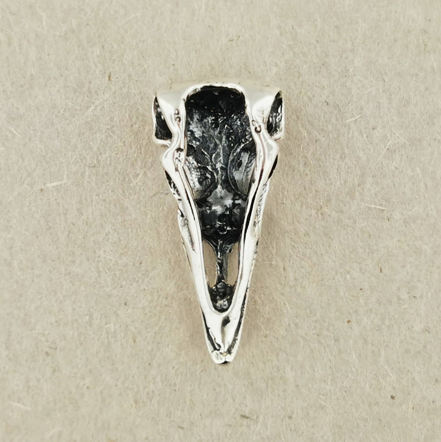 back of  .925 Silver bird skull pendant on a beige background