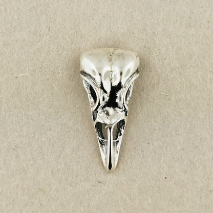 Silver bird skull pendant on a beige background. Sterling silver raven skull charm pendant with gothic and witchy style vibes