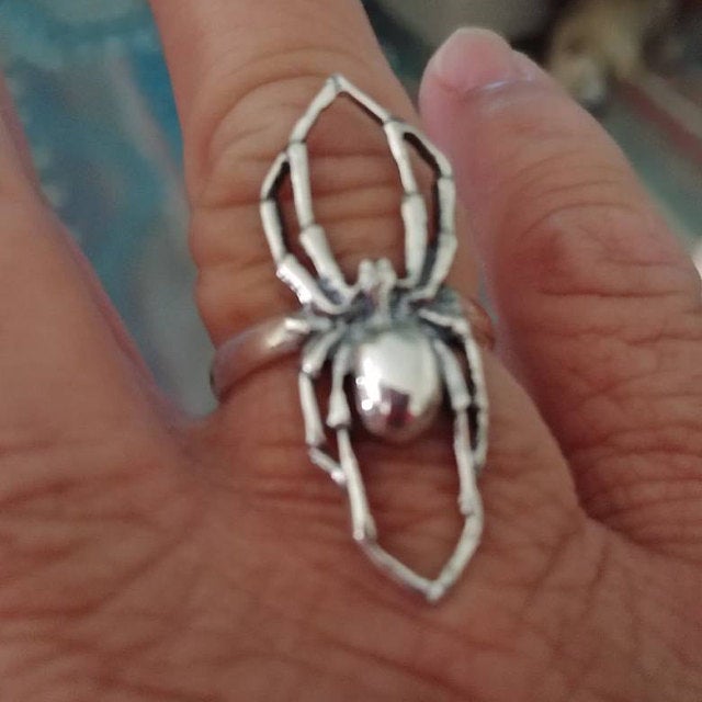 A close-up of a person's hand wearing a silver ring with a detailed spider design.