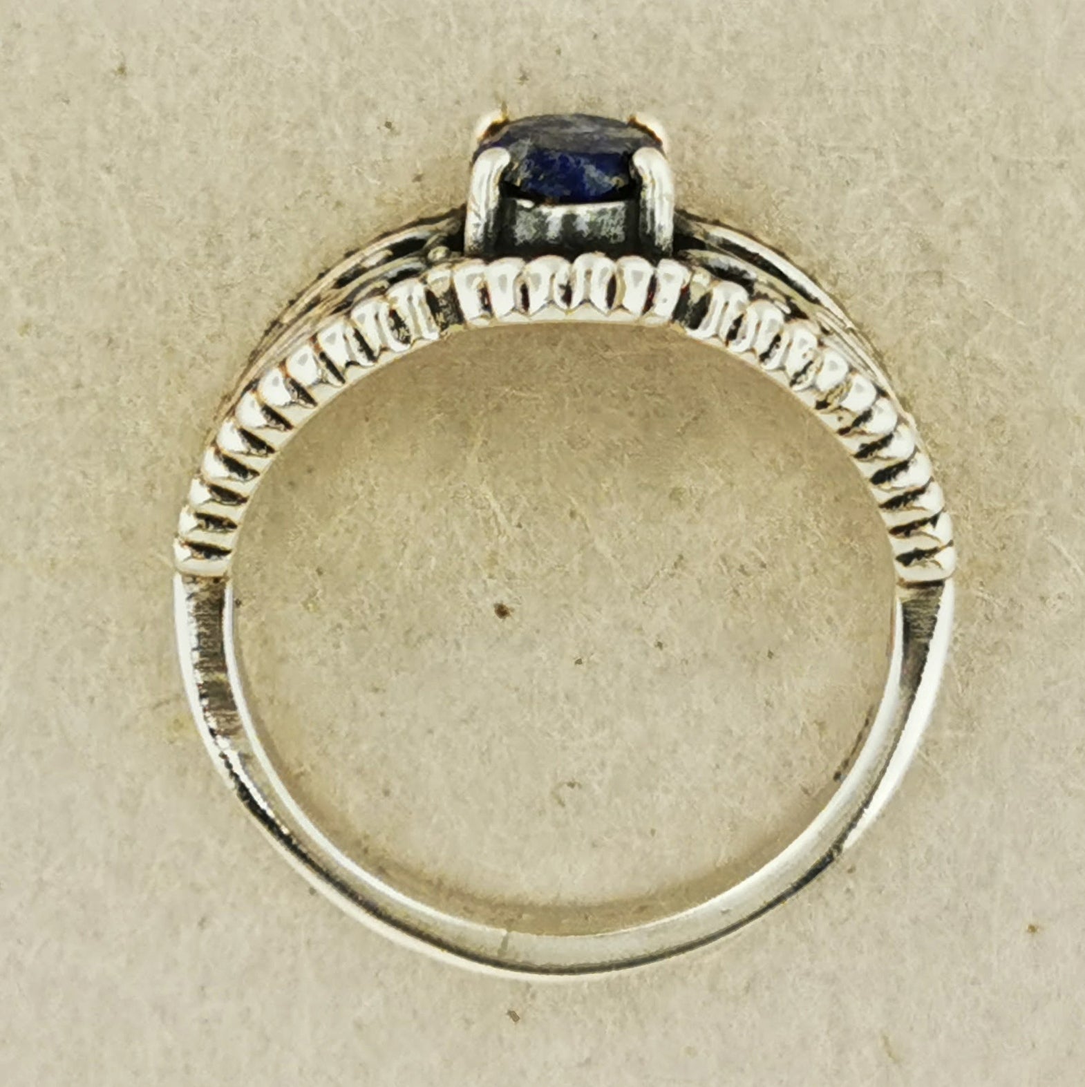 A silver ring with a blue gemstone, possibly a sapphire, set in a decorative band.