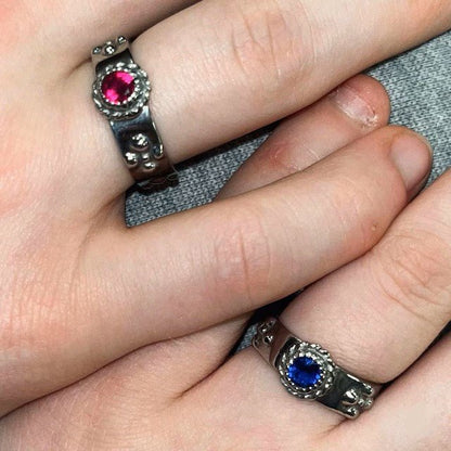 Two silver rings with gemstones are being held together by a person's fingers.
